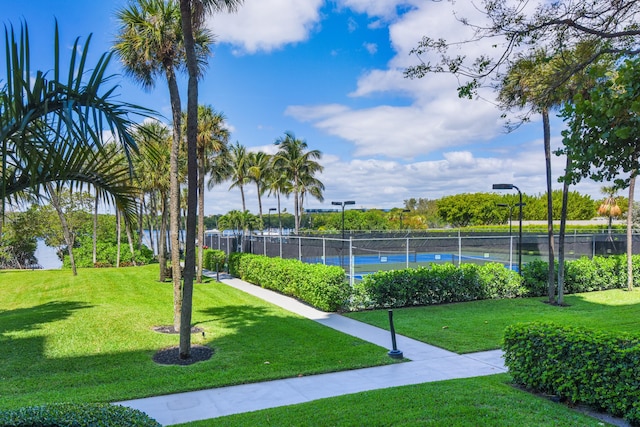 view of property's community featuring a lawn and tennis court