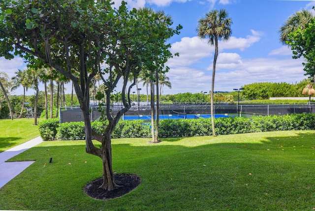 view of community featuring a water view, a lawn, and tennis court