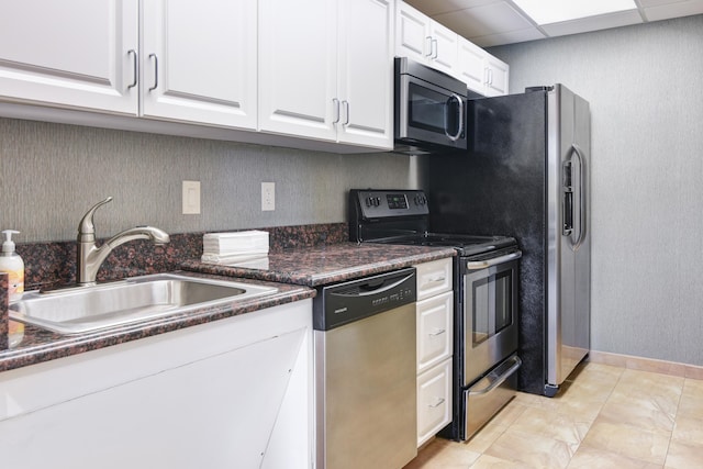 kitchen featuring appliances with stainless steel finishes, a drop ceiling, dark stone counters, sink, and white cabinets