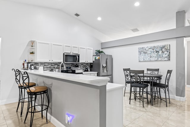 kitchen with stainless steel appliances, vaulted ceiling, white cabinets, kitchen peninsula, and a breakfast bar