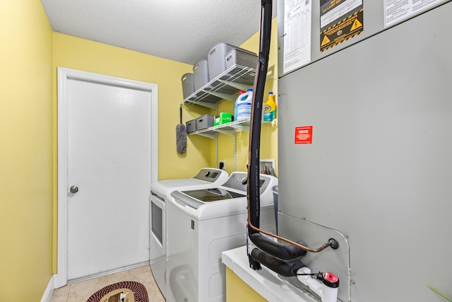 clothes washing area with a textured ceiling, washer and clothes dryer, and light tile patterned floors