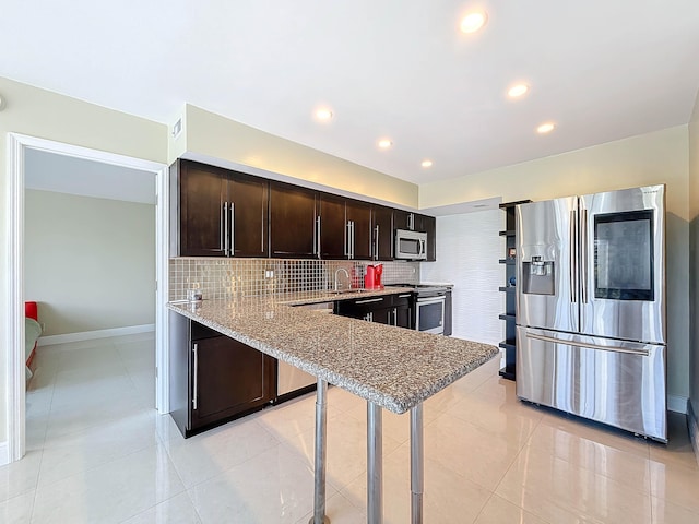 kitchen with appliances with stainless steel finishes, backsplash, light tile patterned floors, and dark brown cabinetry