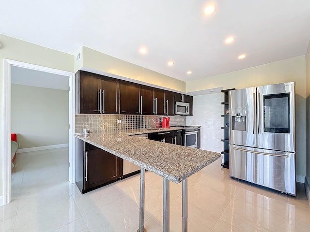 kitchen with light stone countertops, light tile patterned floors, appliances with stainless steel finishes, tasteful backsplash, and dark brown cabinets