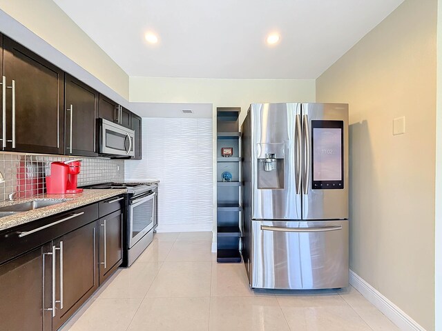 kitchen with sink, stainless steel appliances, light stone counters, dark brown cabinets, and light tile patterned floors