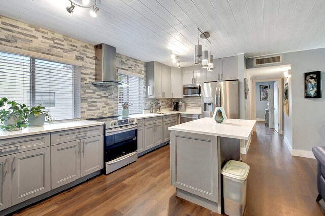 kitchen featuring gray cabinetry, wall chimney range hood, stainless steel appliances, and hanging light fixtures