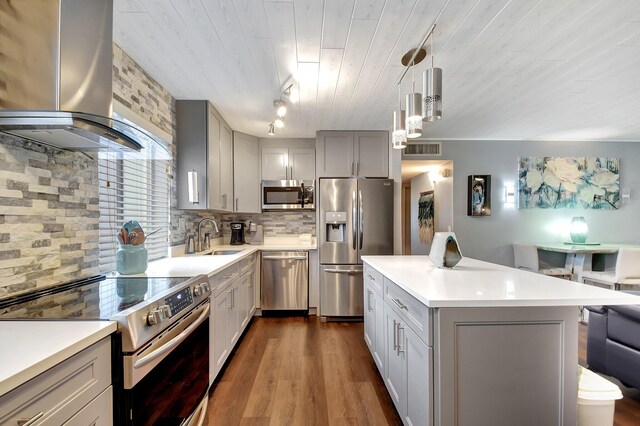 kitchen with wall chimney exhaust hood, stainless steel appliances, dark hardwood / wood-style floors, gray cabinets, and decorative backsplash