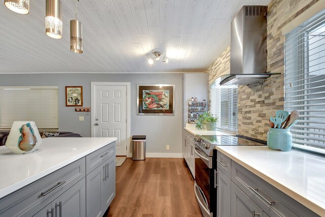 kitchen with a healthy amount of sunlight, stainless steel electric range oven, pendant lighting, and wall chimney range hood