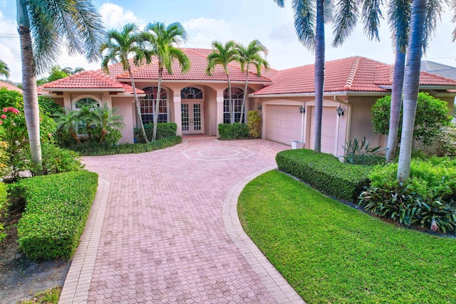 mediterranean / spanish house with a garage, french doors, and a front lawn