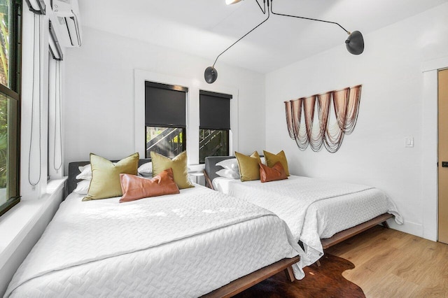 bedroom featuring hardwood / wood-style floors, multiple windows, and an AC wall unit