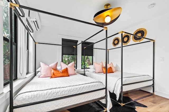 bedroom with an AC wall unit, multiple windows, and wood-type flooring