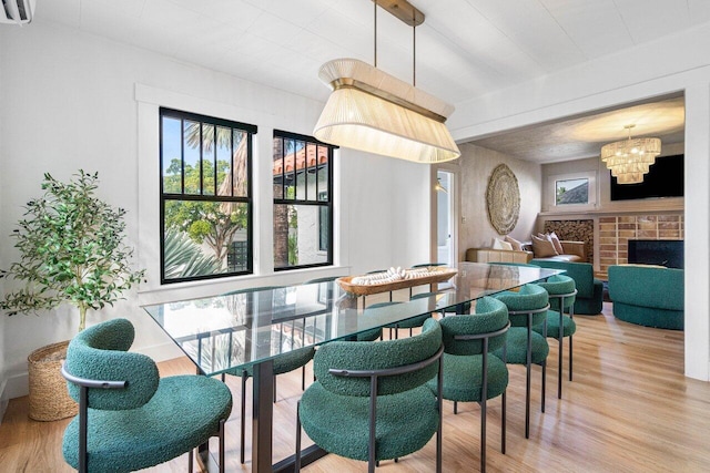 dining area featuring a brick fireplace, light hardwood / wood-style flooring, a wall mounted air conditioner, and an inviting chandelier