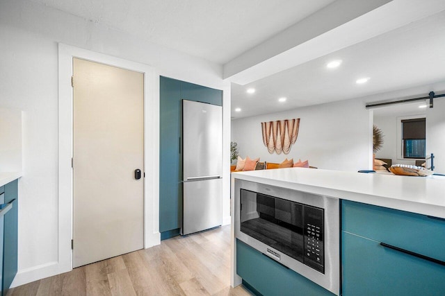 kitchen with light wood-type flooring, stainless steel appliances, and a barn door