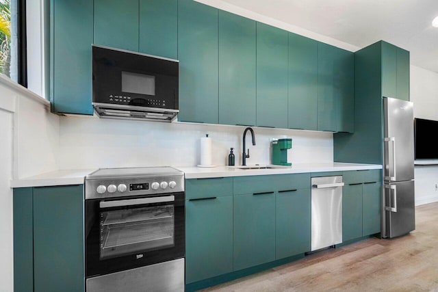 kitchen featuring stainless steel appliances, light wood-type flooring, backsplash, green cabinetry, and sink