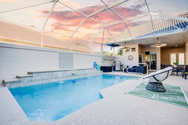 pool at dusk with glass enclosure, ceiling fan, and a patio area