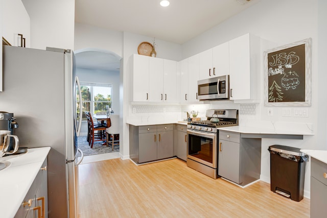 kitchen featuring stainless steel appliances, tasteful backsplash, gray cabinets, white cabinetry, and light wood-type flooring