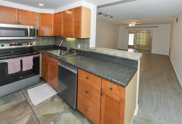 kitchen with appliances with stainless steel finishes, a textured ceiling, decorative backsplash, sink, and kitchen peninsula