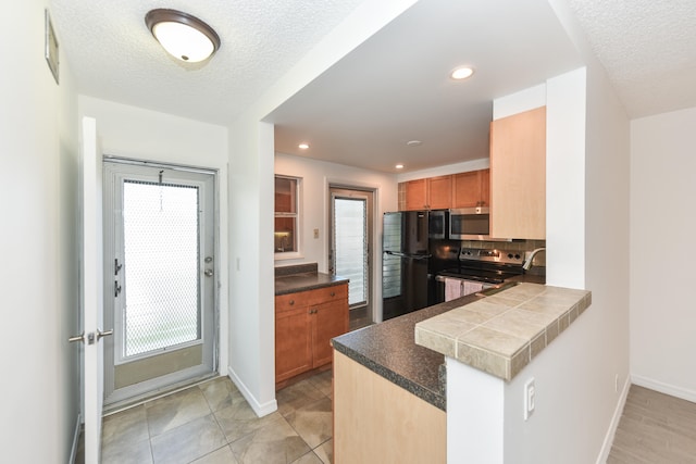 kitchen featuring stainless steel appliances, kitchen peninsula, a textured ceiling, light tile patterned floors, and decorative backsplash