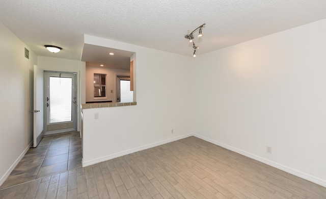 empty room with wood finished floors, a textured ceiling, baseboards, and recessed lighting