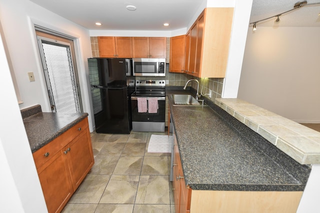 kitchen with stainless steel appliances, a sink, decorative backsplash, dark countertops, and a peninsula