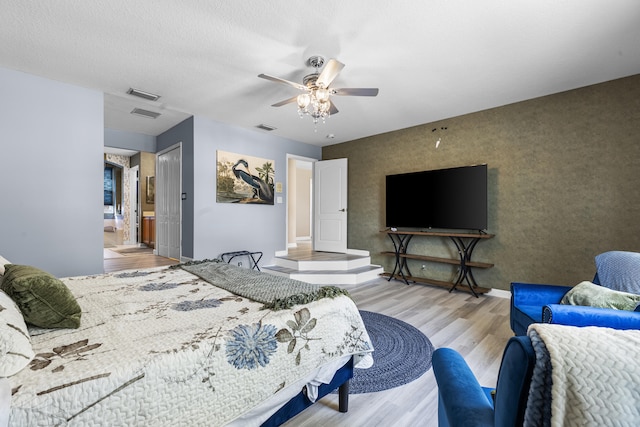 bedroom with light wood-type flooring, a textured ceiling, ceiling fan, and ensuite bath