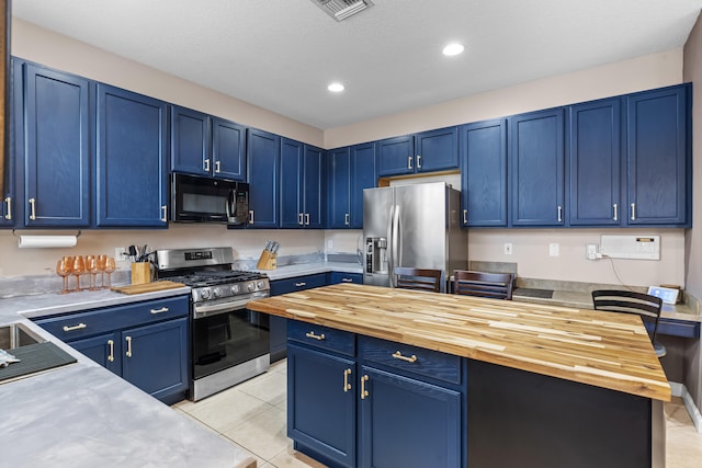 kitchen with stainless steel appliances, blue cabinetry, butcher block counters, and light tile patterned floors