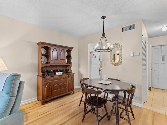 dining room featuring a textured ceiling, light hardwood / wood-style flooring, and a notable chandelier