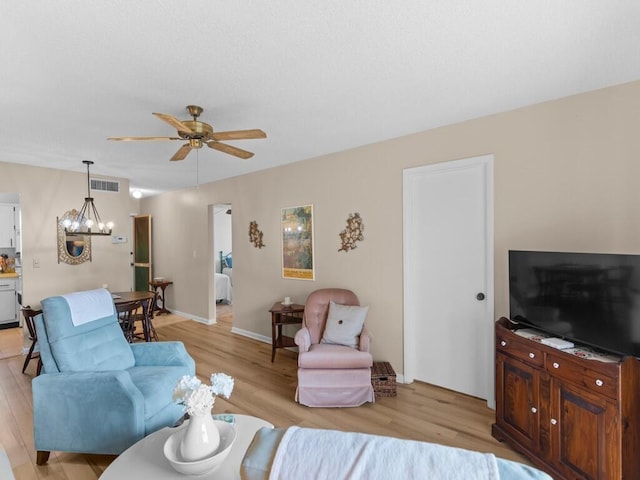 living room featuring ceiling fan with notable chandelier and light hardwood / wood-style flooring