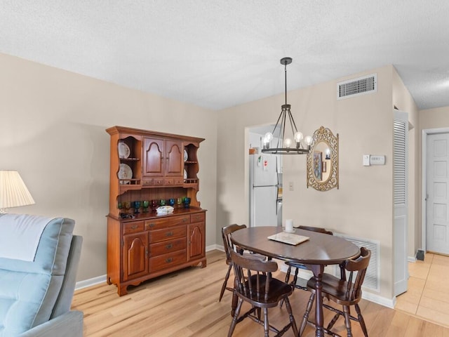 dining room featuring a textured ceiling, a notable chandelier, and light hardwood / wood-style floors