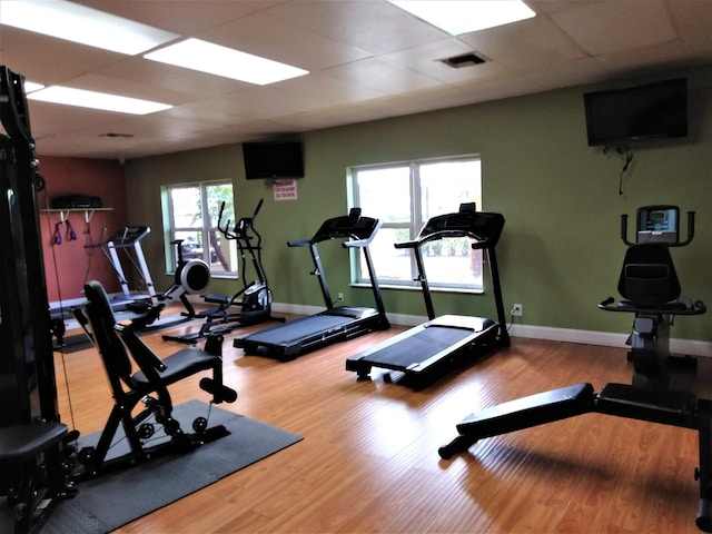 exercise room featuring wood finished floors, a paneled ceiling, and baseboards