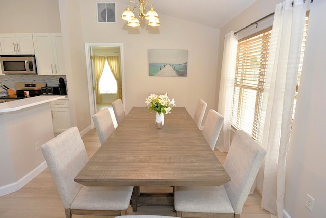 dining space with light wood-type flooring, vaulted ceiling, and a notable chandelier