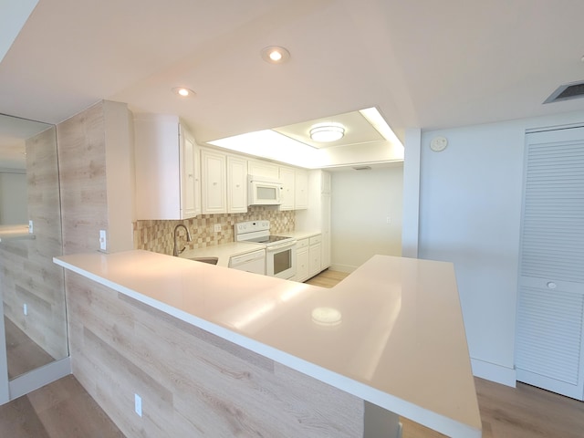 kitchen featuring white cabinets, kitchen peninsula, light hardwood / wood-style floors, and white appliances