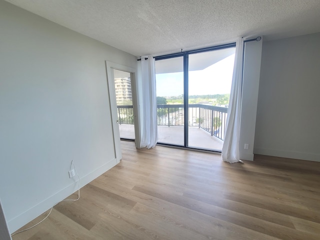 empty room with expansive windows, a textured ceiling, and light hardwood / wood-style flooring