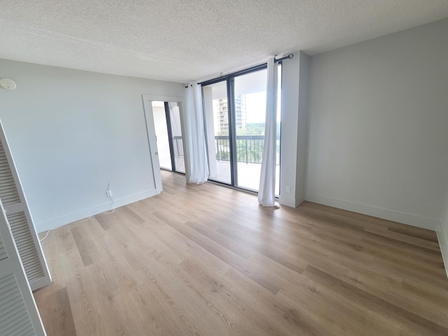 spare room with light wood-type flooring, a wall of windows, and a textured ceiling