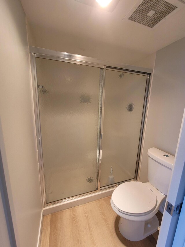 bathroom with hardwood / wood-style floors, a shower with shower door, and toilet