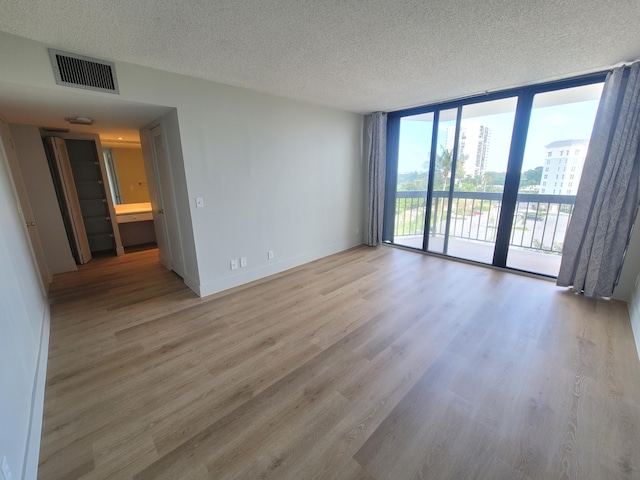 unfurnished room featuring floor to ceiling windows, a textured ceiling, and light hardwood / wood-style floors