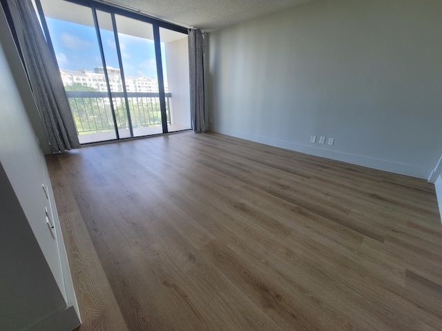 unfurnished room with a textured ceiling, a wealth of natural light, wood-type flooring, and a wall of windows