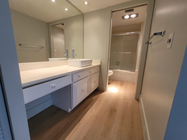 full bathroom with toilet, vanity, hardwood / wood-style floors, and shower / bath combination with glass door