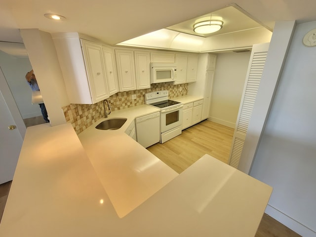 kitchen with tasteful backsplash, white appliances, sink, kitchen peninsula, and light hardwood / wood-style flooring