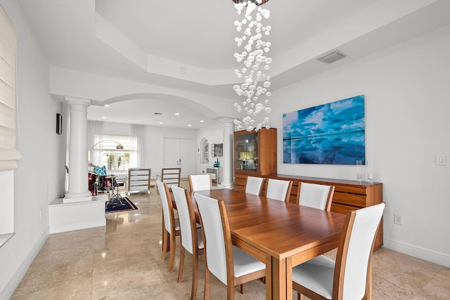 dining room with a notable chandelier, a tray ceiling, and decorative columns