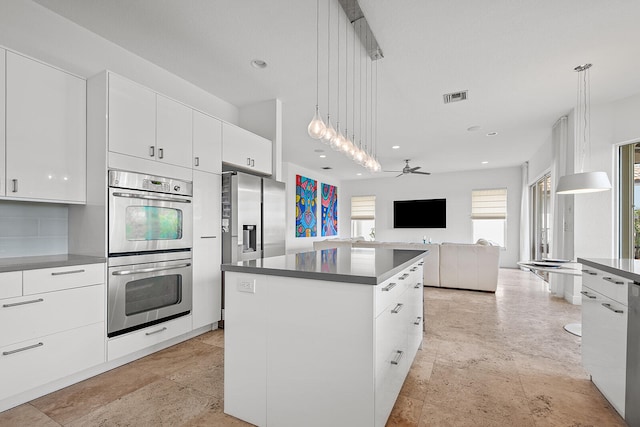 kitchen with pendant lighting, ceiling fan, appliances with stainless steel finishes, a kitchen island, and white cabinetry