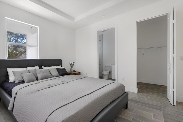 unfurnished bedroom featuring ensuite bath, light wood-type flooring, and a walk in closet