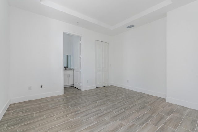 unfurnished bedroom with baseboards, visible vents, wood finish floors, a tray ceiling, and connected bathroom