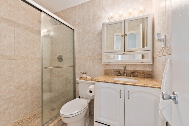 bathroom with a textured ceiling, vanity, a shower with door, tile walls, and toilet