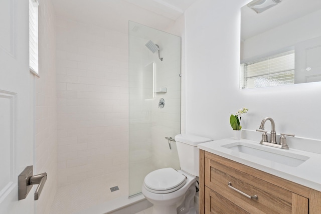 bathroom featuring a tile shower, vanity, and toilet