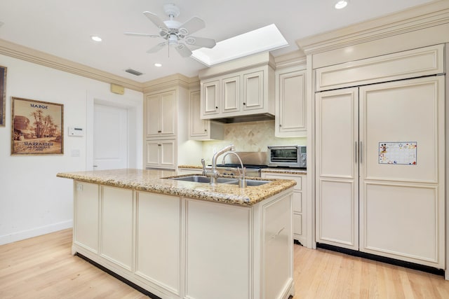 kitchen with a center island with sink, light stone counters, a skylight, light hardwood / wood-style flooring, and cream cabinetry