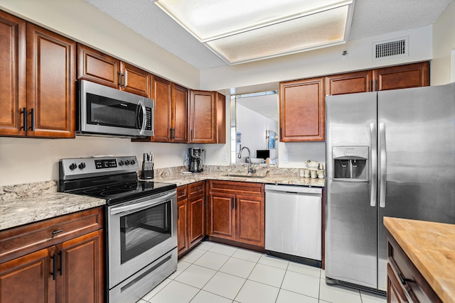 kitchen with wooden counters, sink, light tile patterned floors, a textured ceiling, and stainless steel appliances