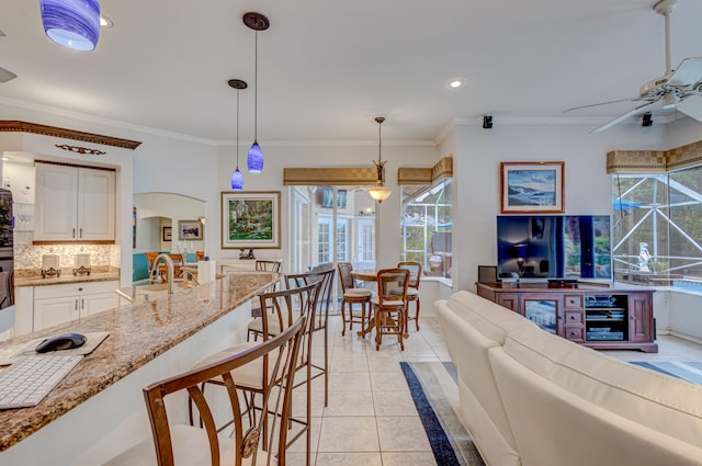 tiled living room featuring plenty of natural light, ceiling fan, crown molding, and sink