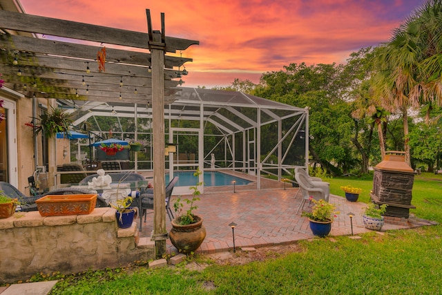 pool at dusk with glass enclosure, a patio area, a lawn, and a jacuzzi