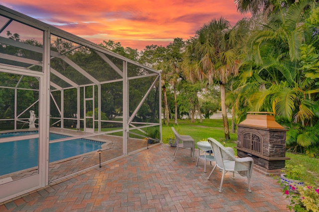 pool at dusk featuring glass enclosure and a patio area