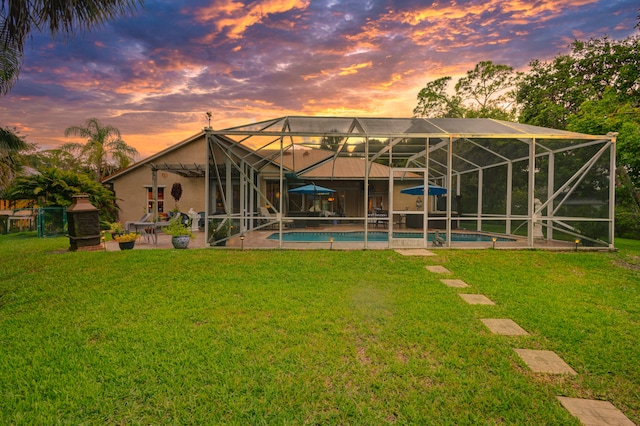 back house at dusk featuring a lawn, glass enclosure, and a patio